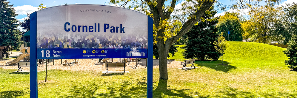 Cornell Park's sign with grass, trees and a playground in the background.
