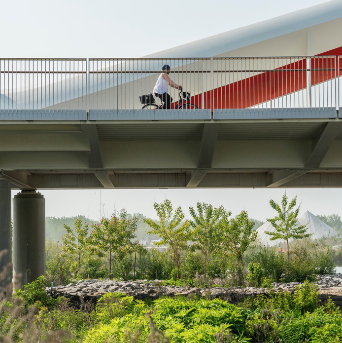 A person rides a bike on a bridge over a naturalized landscape.