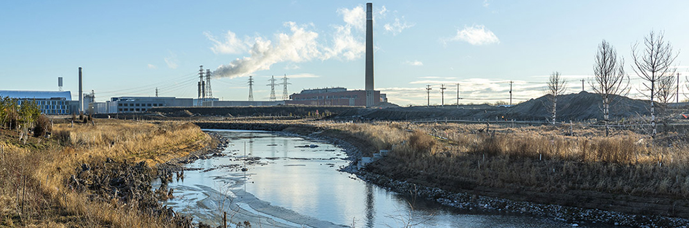 An industrial skyline with curved river and some renaturalized land in front.