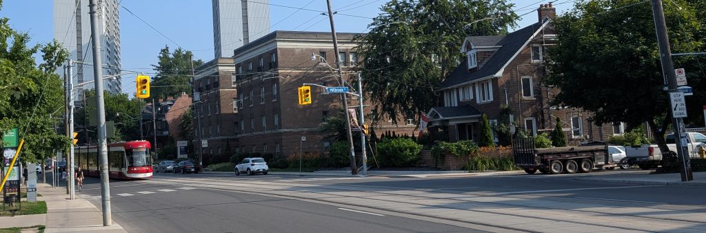 Intersection pedestrian signal at Millbrook Cres and Broadview Ave. The photo depicts a signal at the north side of the intersection that controls north and south movements along Broadview Ave and pedestrian movements across the street. People cycling and driving and turning from Millbrook are to use the stop sign and only proceed onto Broadview Ave when it is safe to do so.