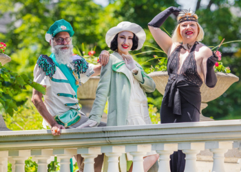 Three people wearing 1920s costumes pose outside in a garden.