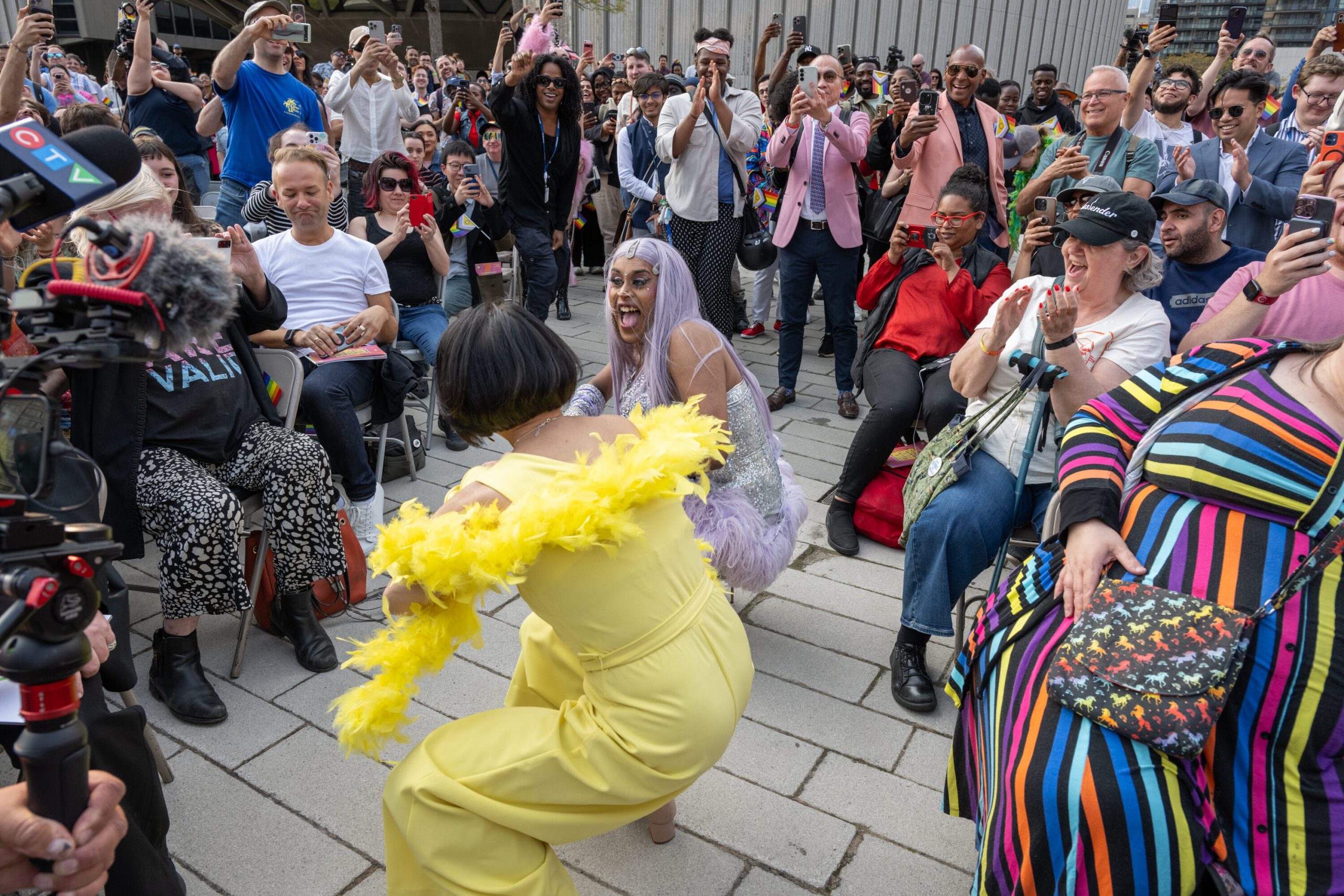 A crowd of people watching a drag performer, Sanjina DaBish Queen, and Toronto Mayor Olivia Chow dance outside of Toronto City Hall.