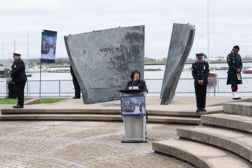 Speaker at a podium, memorial in the background