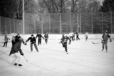 A group of teens play ice hockey outdoors at a park.