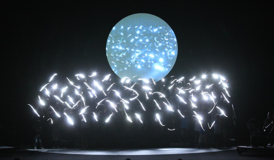 Group of people with bright light smudges above each person, all standing in front of an orb with speckles of light