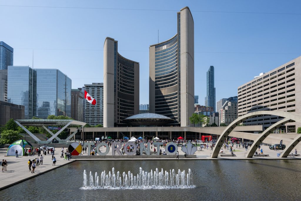 Toronto City Hall and the TORONTO sign behind the fountain and reflecting pool on a sunny day