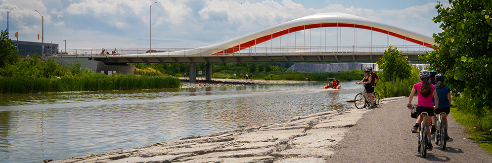 A walkway next to a river with a bridge in the distance.