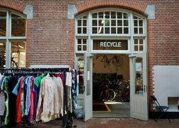 Building with a door with a white frame reading recycle at the top with a rack of clothes to the left.