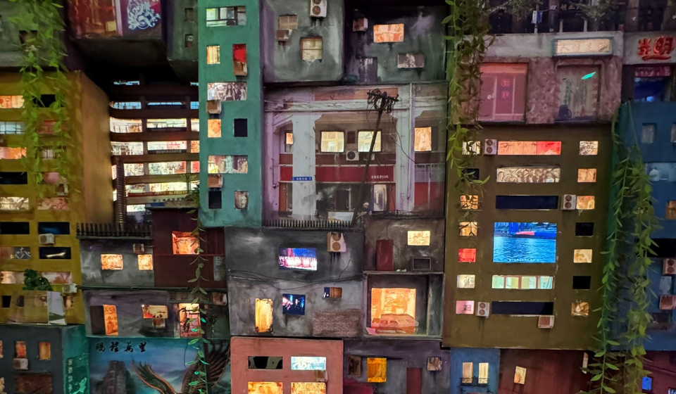 Artwork of variety of stacked miniature urban buildings with lit windows.