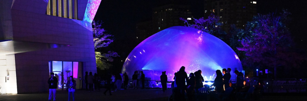 Silhouettes of people in front of projected light artworks on building and dome