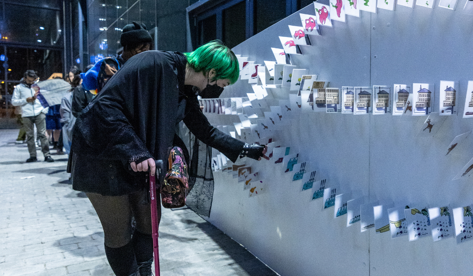 Person using a cane reaches down to touch cards perpendicularly sticking out from wall, each with a different illustration.