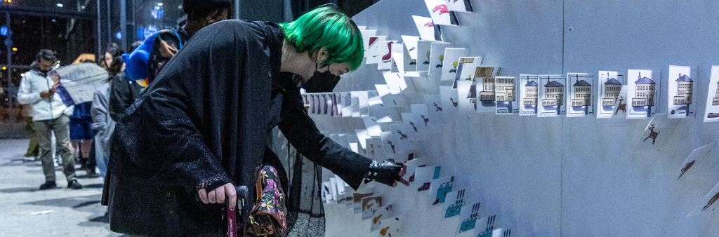 Person using a cane reaches down to touch cards perpendicularly sticking out from wall, each with a different illustration.