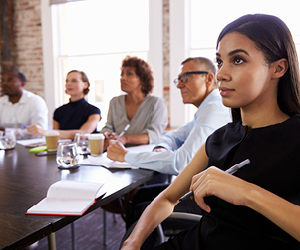 People in a meeting sitting around a boardroom table with notepads and pens.