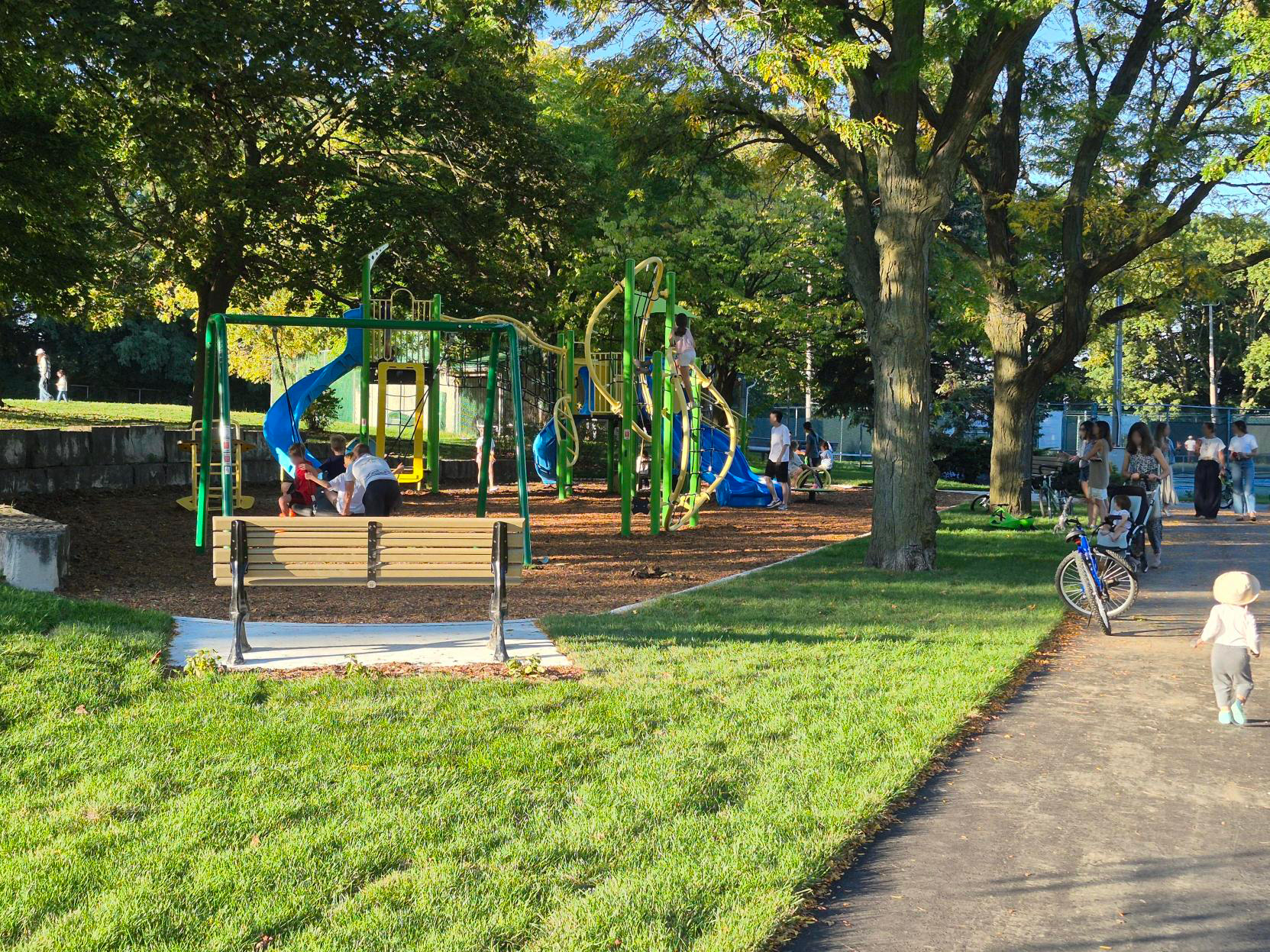 People playing on swings. A brightly coloured playground is in the background.