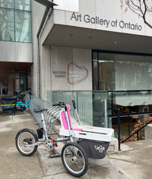 Image of a cargo bike that carries parcels that is pink, white and black. 