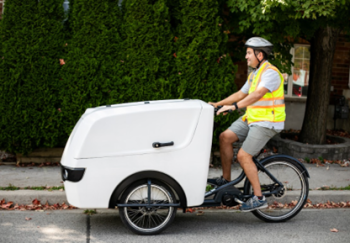 Image of cargo bike with a delivery person riding it. 