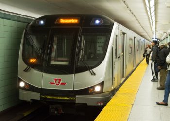To Toronto subway car pulling into a busy station with people on the platform.