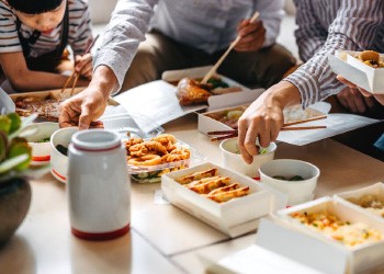 A dinner table with food in takeaway containers and people filling their plates.