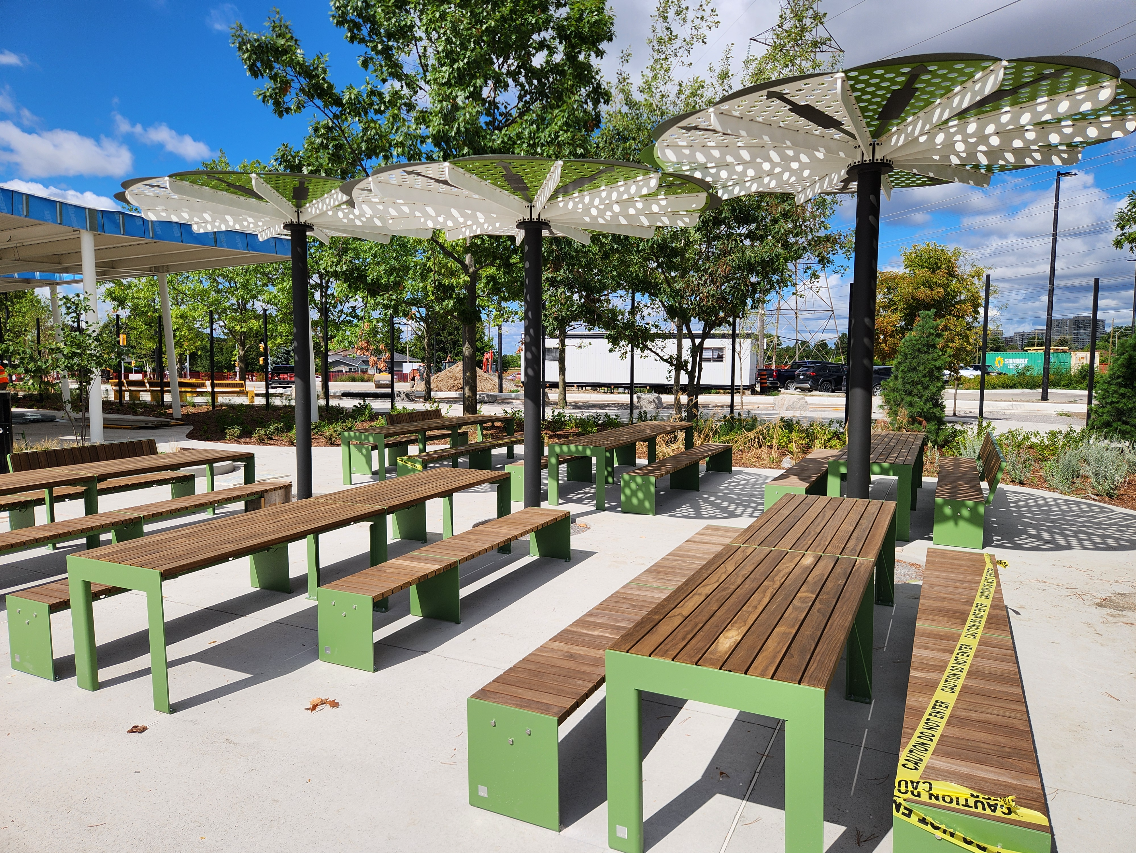 Multiple green picnic tables with brown wooden tops and three large white and green shade structures with black posts.