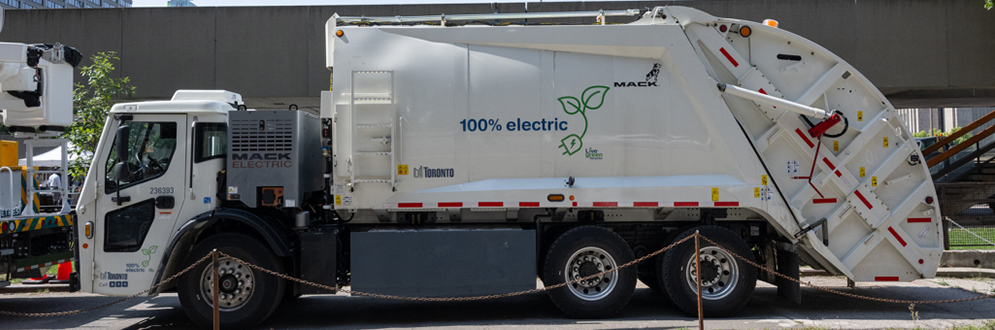 A white garbage truck with a City of Toronto Logo and large text that says "100% electric"