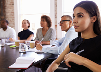 People in a meeting sitting around a boardroom table with notepads and pens.