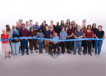 A diverse group of people posing for a group photo with a blue ribbon that reads Toronto in front of them.