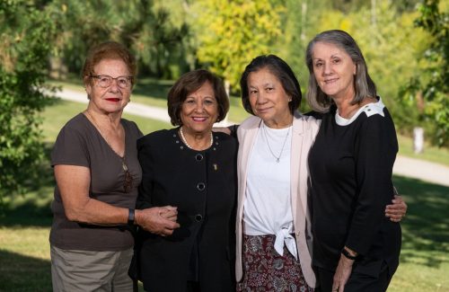 Four senior women holding each other with a green nature backdrop