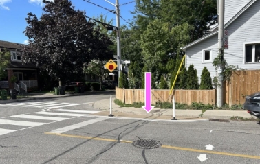 Photo showing an example of a curb extension with bollards. The pink arrow identifies the planned painted area.