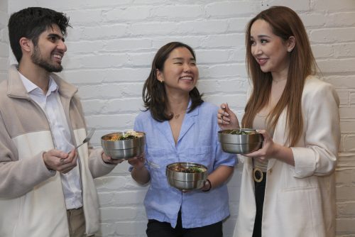 A group of three people holding insulated reusable containers full of food.