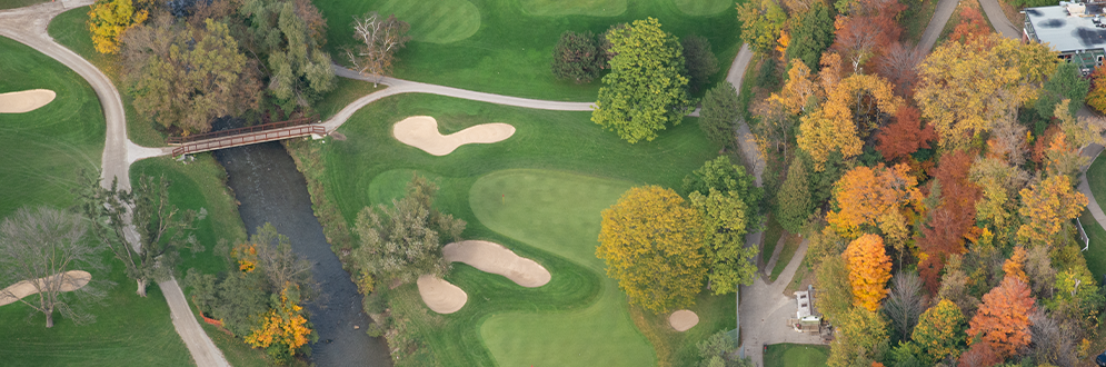 Aerial view of a golf course bordered by a river and colorful autumn trees.