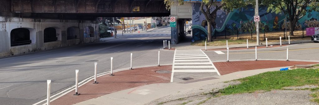 Quick Build Safety Improvement project at the intersection of Carlaw Ave and Gerrard St E. Quick build projects use materials such as paint and bollards to realize the safety benefits of an intersection redesign in advance of a permanent intersection reconfiguration.