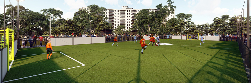 Ground-level view from one end of the field, capturing players in action near a goal. Trees and buildings are visible in the background, adding context to the urban setting.