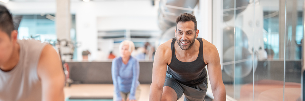 A group of people indoors in a fitness class with weights and step up blocks.