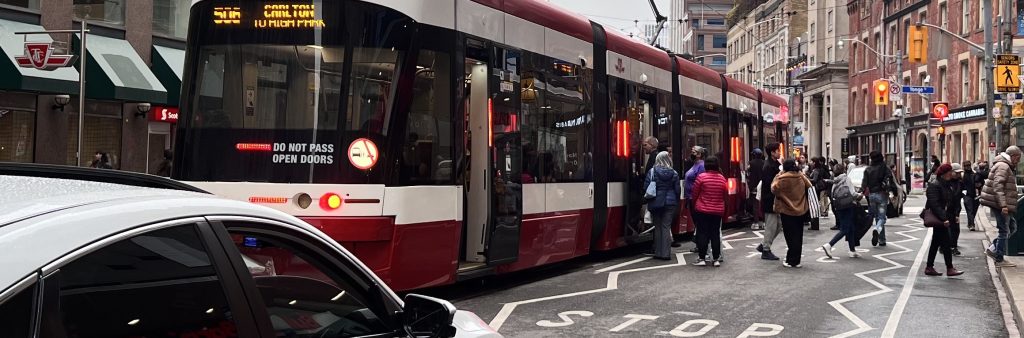 Enhanced pavement markings at the streetcar stop on College St at Yonge St. The pavement markings include zig zag pavement markings along the stop area and advance warning messages for the upcoming transit stop.