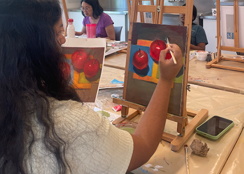 Person painting a picture of apples in an art classroom