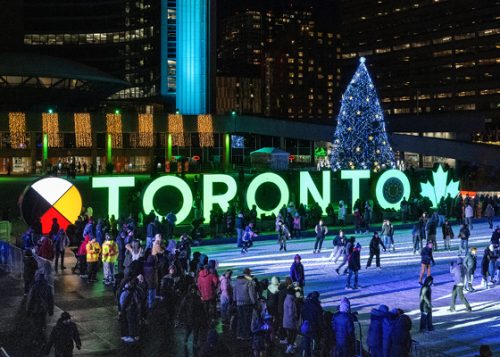Nathan Phillips Square lit up at night with skaters on skating rink, the Toronto sign and Christmas tree