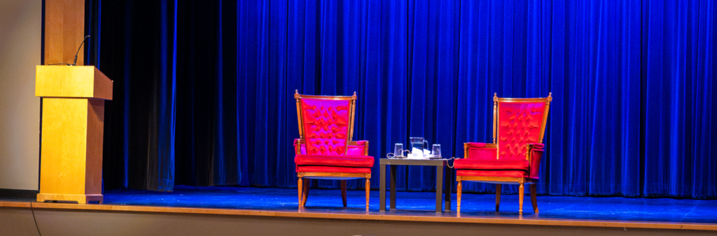 Two ornate red chairs centered on theatre stage with a podium on the left