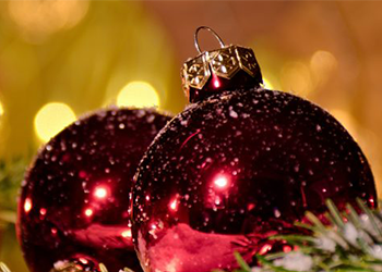 Two red holiday ornaments with gold blurred lights in background.
