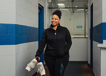 A person walking in a hallway holding a pair of figure skates.