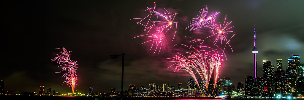 Pink fireworks in the night sky in Toronto's inner harbour with the city skyline in the background.