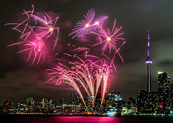 Bright pink fireworks in the night sky over the lake with the Toronto downtown skyline in the background.