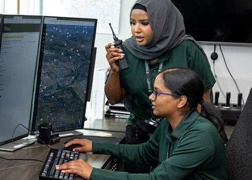 A crisis support worker talking into a walkie-talkie and the other sitting at a desk typing as they look at computer screens.
