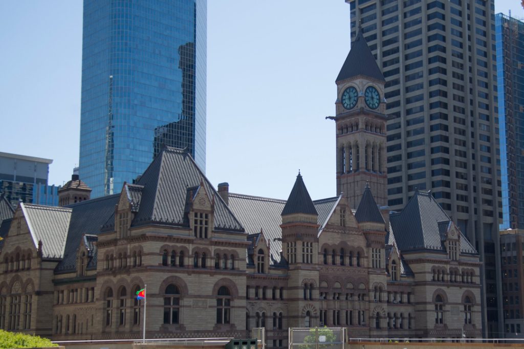 Exterior view of Old City Hall in Toronto, featuring its arched windows, and tall clock tower against a blue sky.