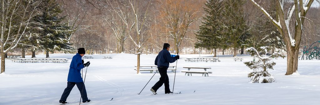 A couple snow-walking with skis through snowy Morningside Park.