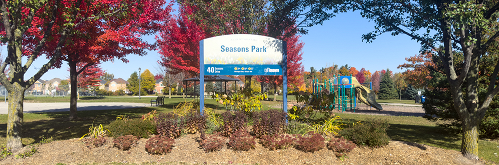 Seasons Park sign with red and green trees in the background.