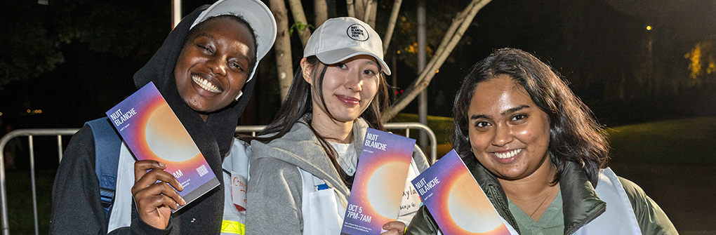 Three volunteers smiling at the camera and holding pamphlets