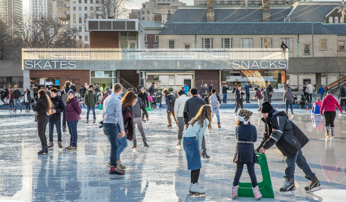 Skaters on ice rink with building behind with signs reading skates and snacks