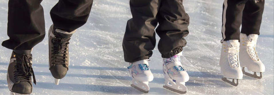 A family group skates together on an outdoor rink, their skates visible as they move across the textured ice.