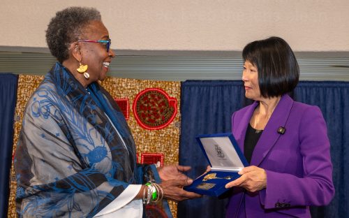 Two women facing each other smiling, one giving a velvet box