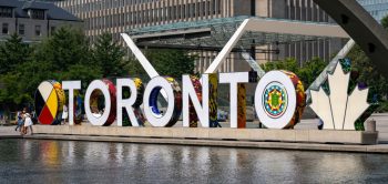Toronto Sign with people standing near letters. Reflecting pool in forground.